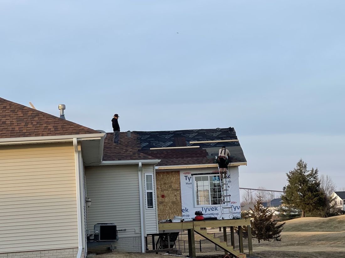 Trego Roofing crew member on a ladder installing shingles
