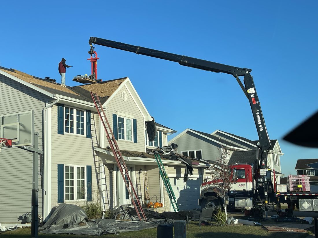 Crane lifting roofing materials to a crew on a roof